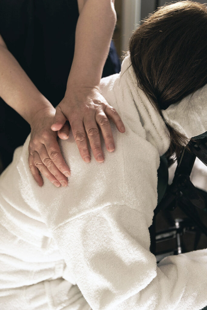 Massage therapies photo of therapist massaging woman's back, neck and shoulders on a chair.